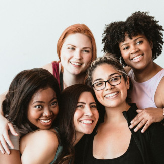 a diverse group of five women  hugging